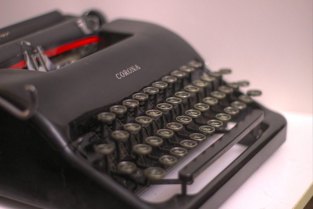 An antique Corona typewriter on a white tabletop.